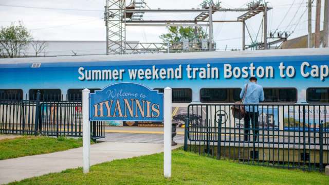 A sign welcomes visitors to Hyannis next to a train advertising services to Cape Cod from Boston.