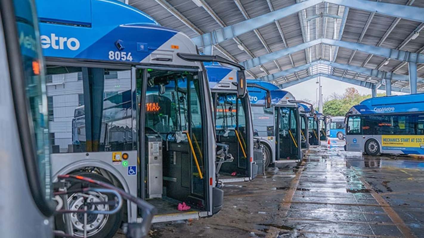 Buses parked in an indoor garage with a covered roof and wet floor.