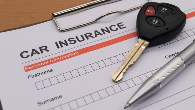 A car key and a pen on a car insurance form with personal information fields.