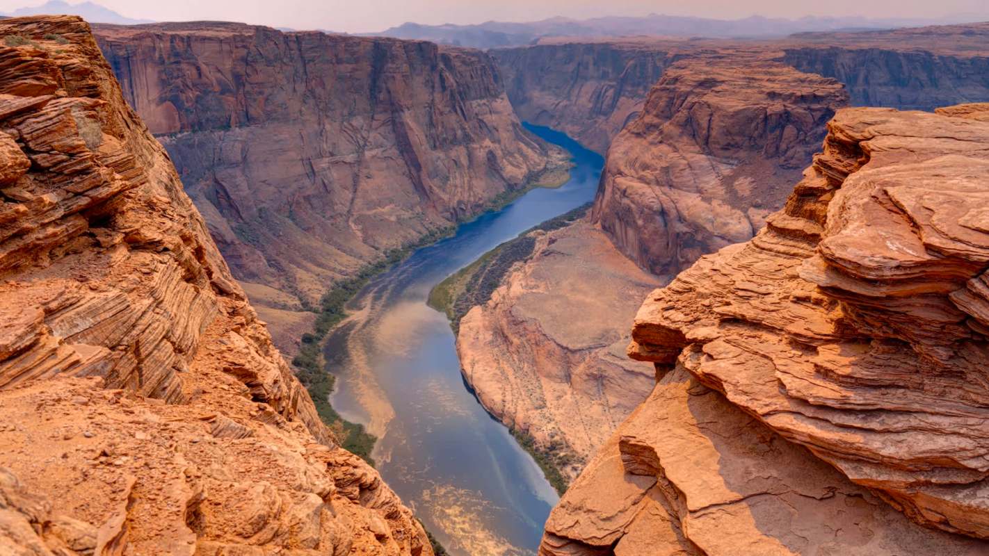 A winding river flows through a canyon with steep reddish-brown cliffs.