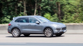 A gray SUV drives on a highway surrounded by greenery.