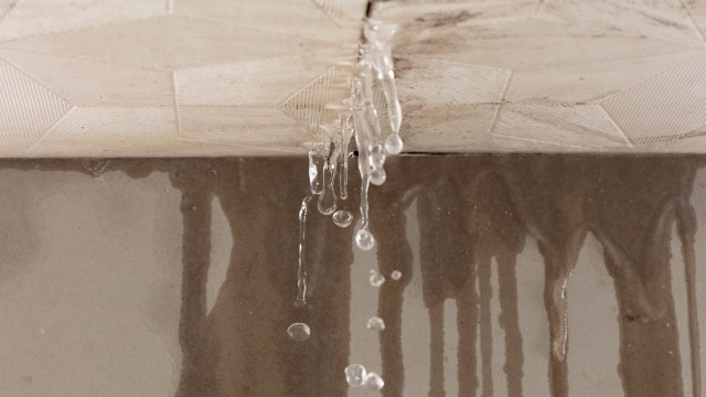 Water drips from a textured ceiling onto a stained surface below.