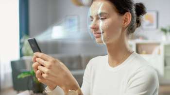 A woman interacts with a smartphone, with a digital face recognition overlay displayed.