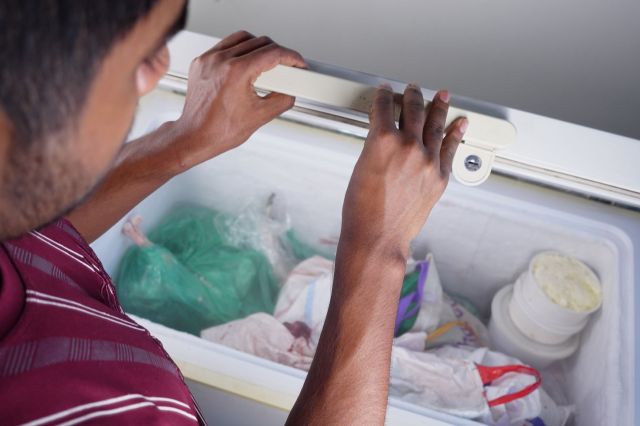 A man opening a chest freezer.