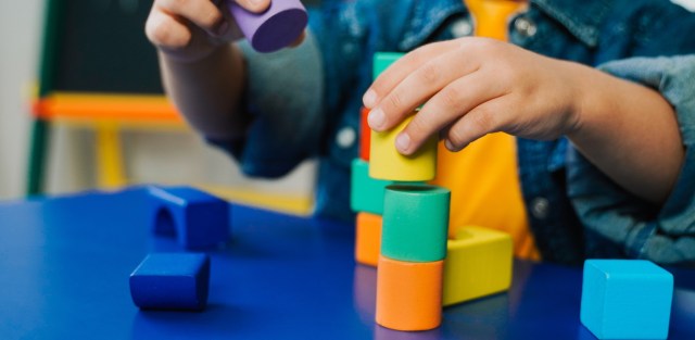 A child stacking colorful blocks on a blue table.