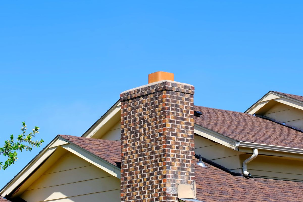 A brick chimney stack on top of a house against a blue sky