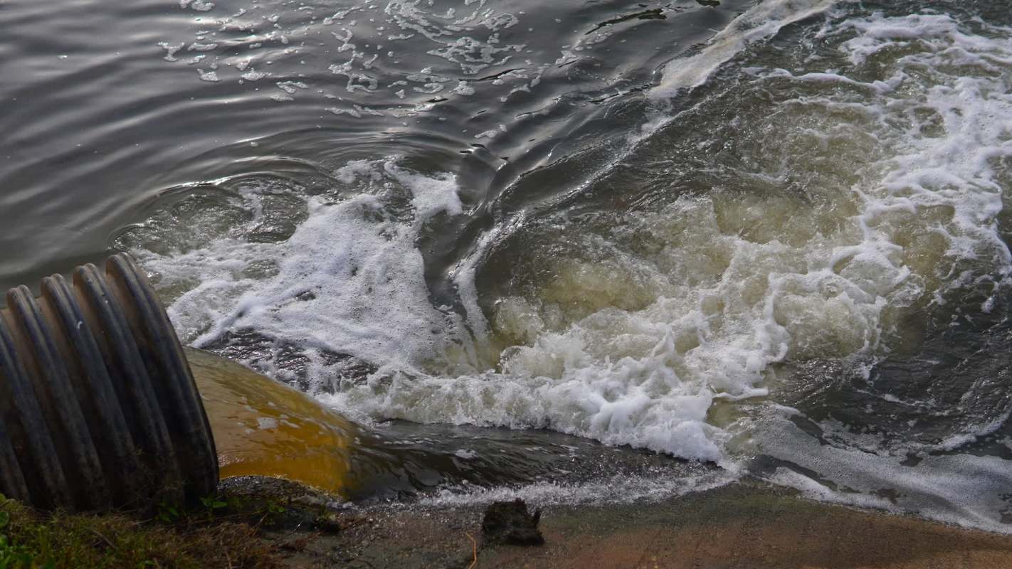 A pipe discharges water into a body of water, creating waves and bubbles.