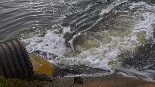 A pipe discharges water into a body of water, creating waves and bubbles.