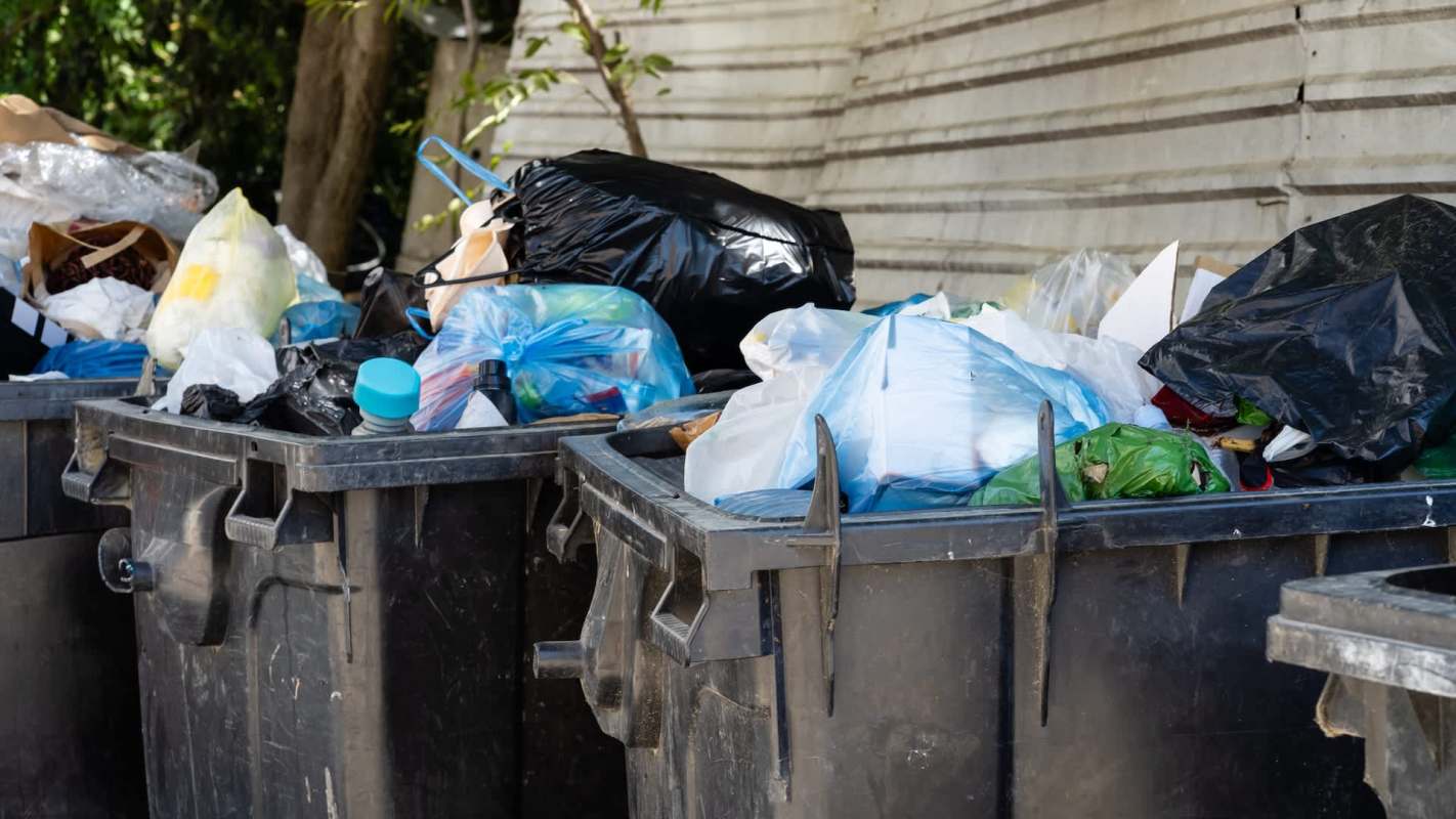 Two trash bins overflowing with various bags of garbage and waste materials.