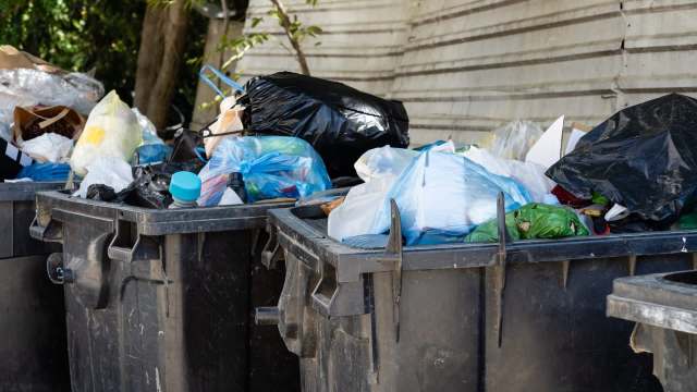 Two trash bins overflowing with various bags of garbage and waste materials.