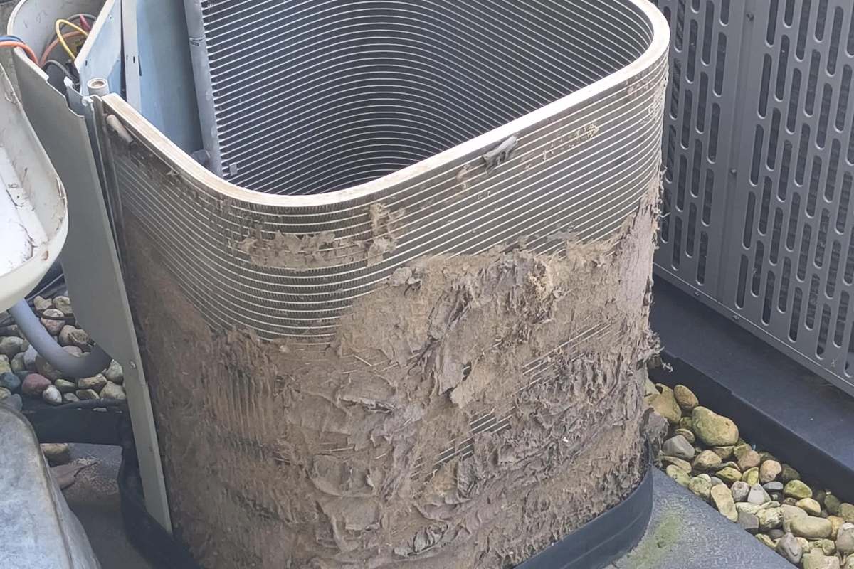 An air conditioning condenser outdoors covered in dirt and debris, showing wear and neglect.