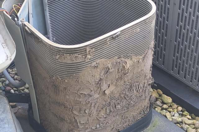 An air conditioning condenser outdoors covered in dirt and debris, showing wear and neglect.