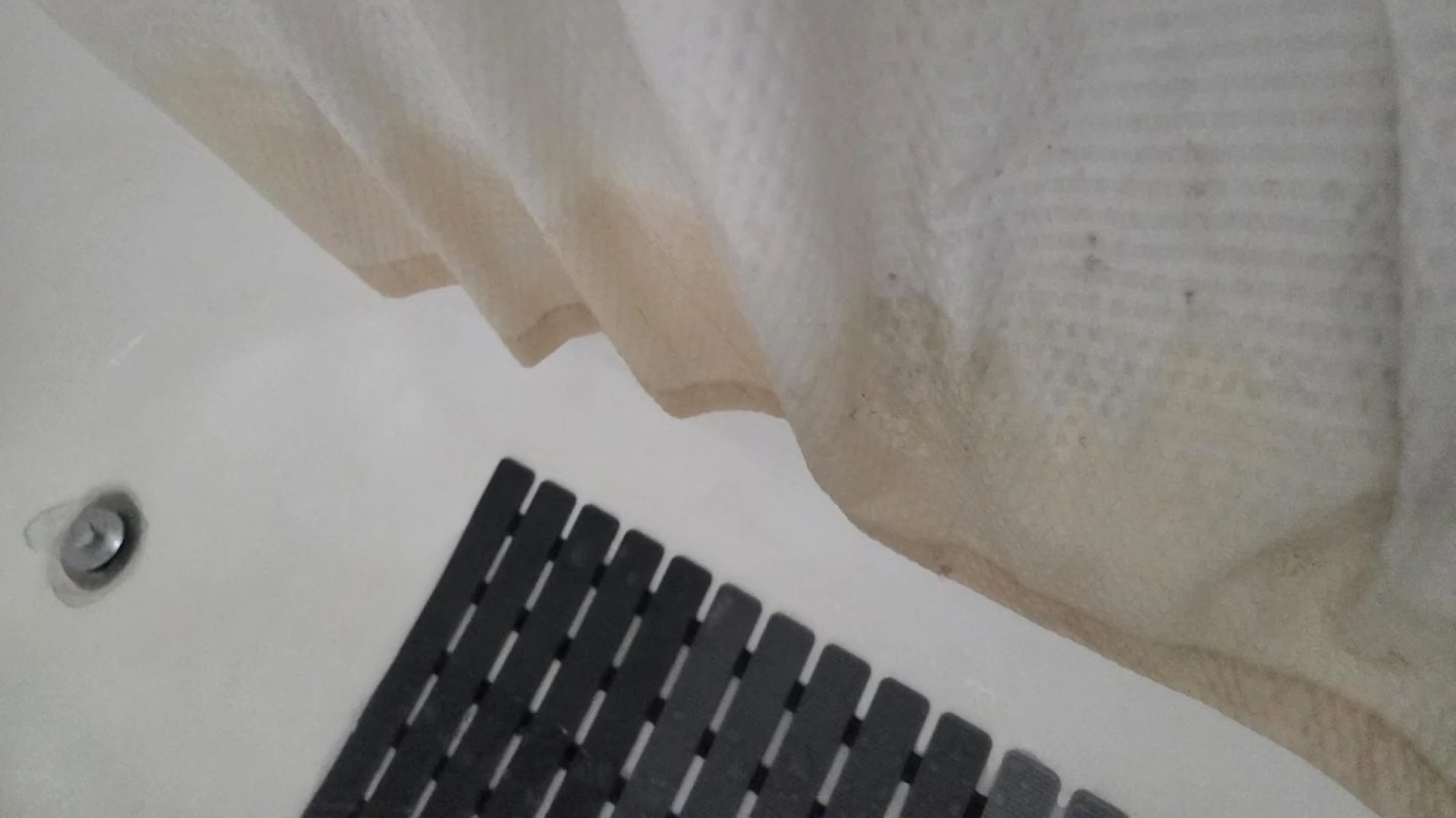 A shower curtain with pink stains and a black bath mat on a tiled floor.