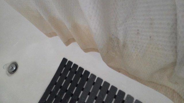 A shower curtain with pink stains and a black bath mat on a tiled floor.