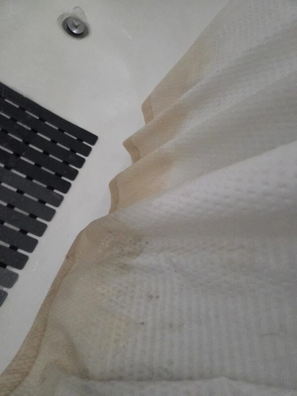 A shower curtain with pink stains and a black bath mat on a tiled floor.
