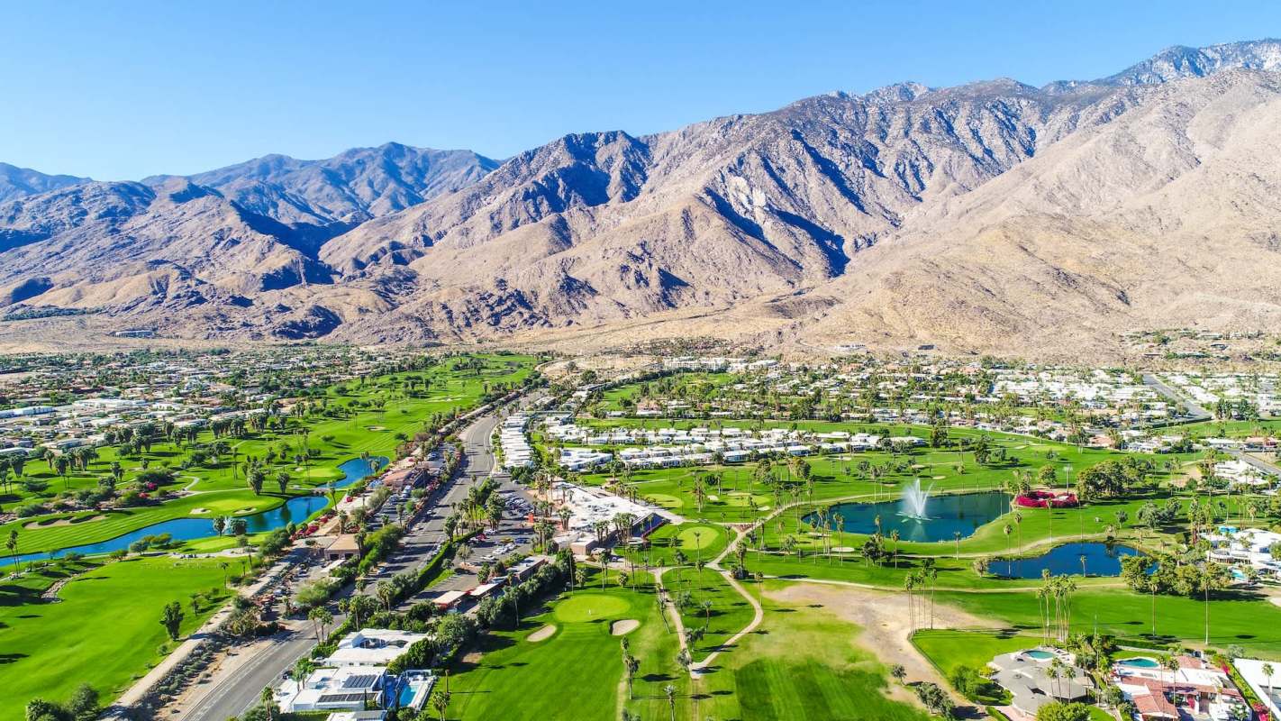 Aerial view of a golf course with water features and mountains in the background.