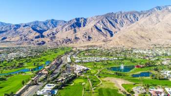 Aerial view of a golf course with water features and mountains in the background.