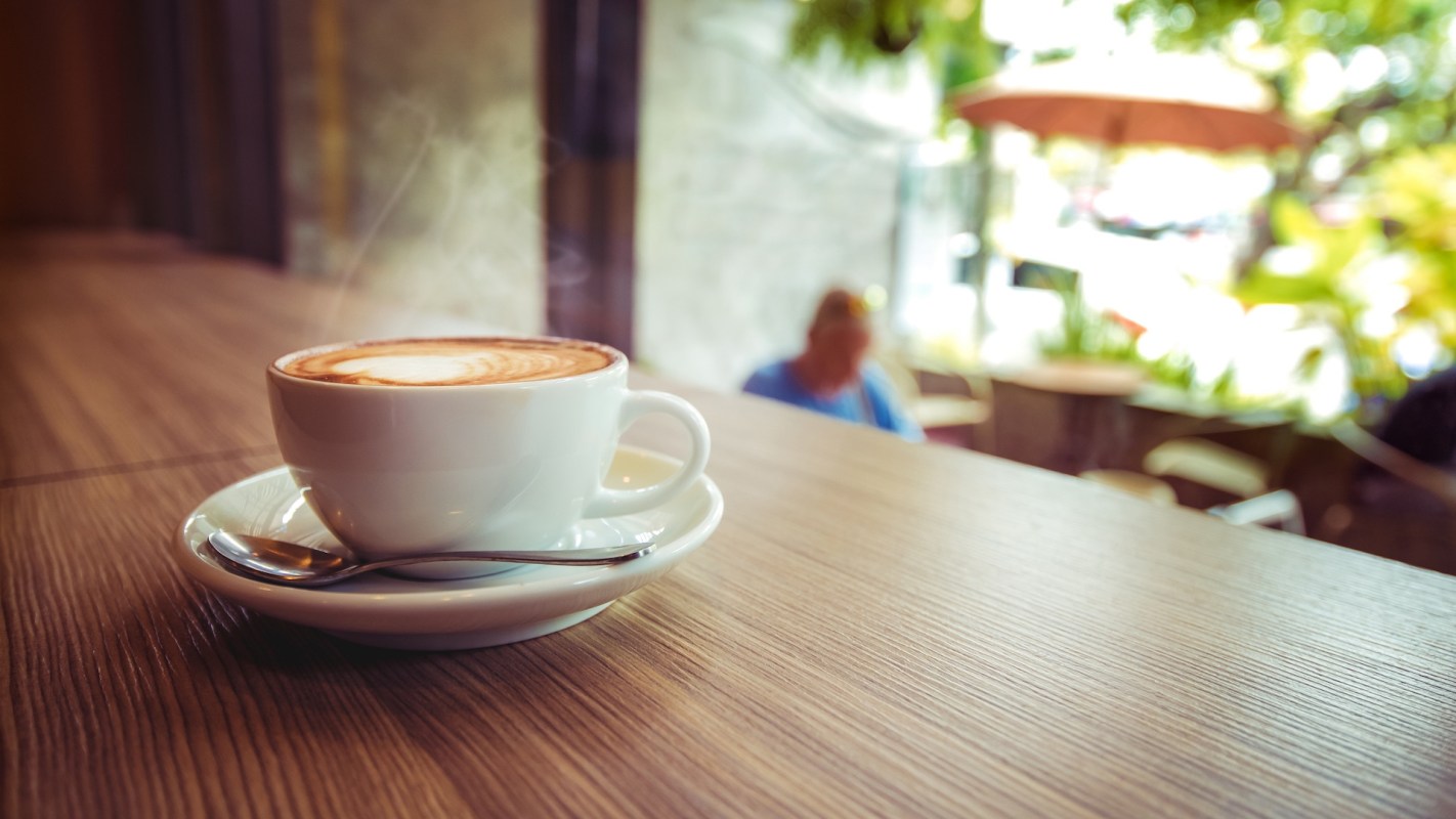A cup of coffee with steam on a wooden table in a café.