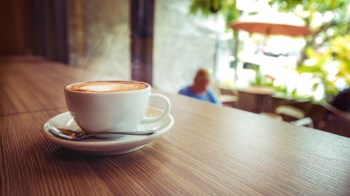 A cup of coffee with steam on a wooden table in a café.