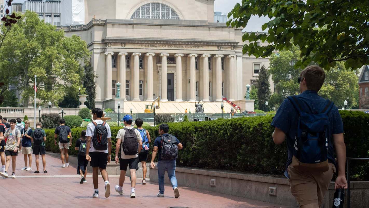 A group of students walks by the Library of Columbia University on a sunny day.