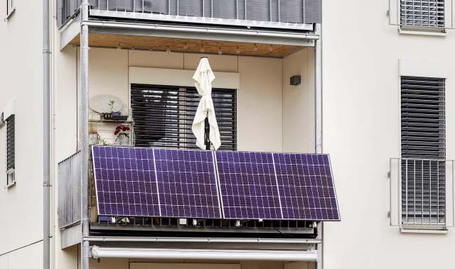 A balcony with solar panels, a white umbrella, and potted plants.