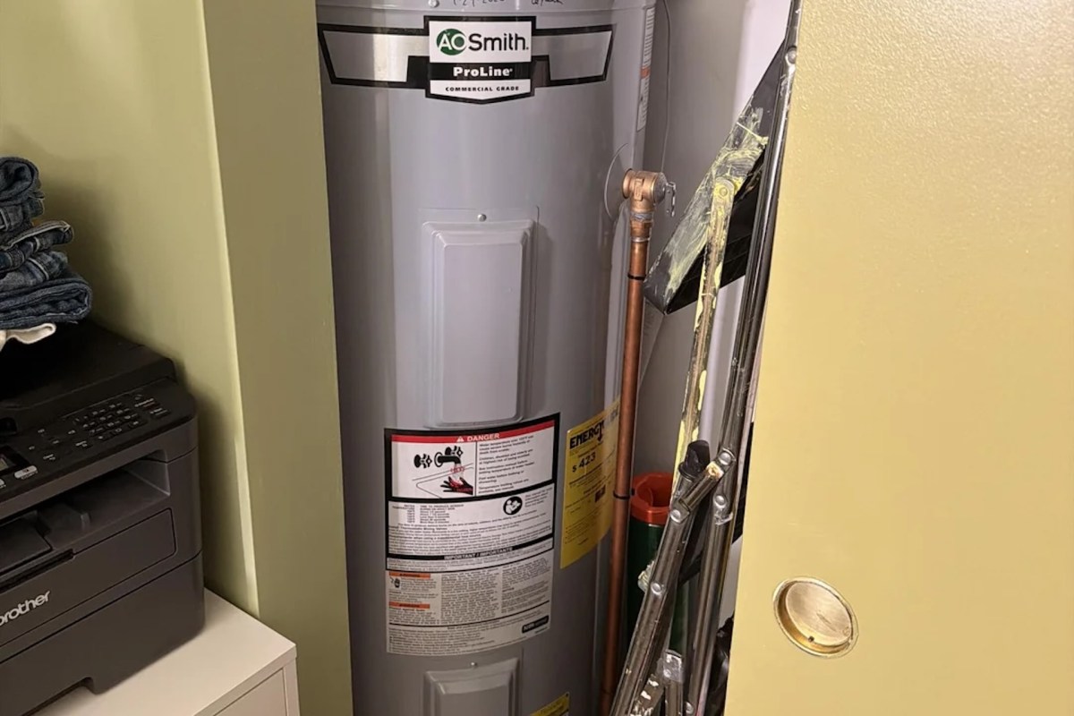 A water heater beside a printer and stacked clothing in a storage area.
