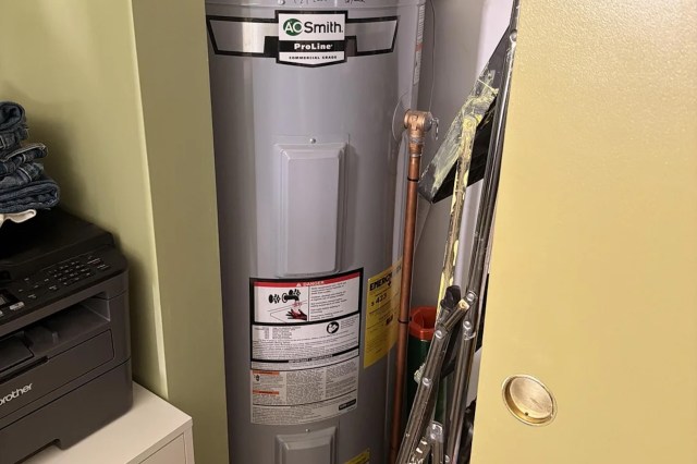 A water heater beside a printer and stacked clothing in a storage area.
