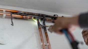 A person is using a torch to solder copper pipes on a wall.
