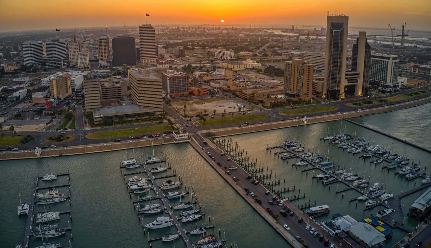 A waterfront view of Corpus Christi, Texas, marina with boats and a skyline at sunset.