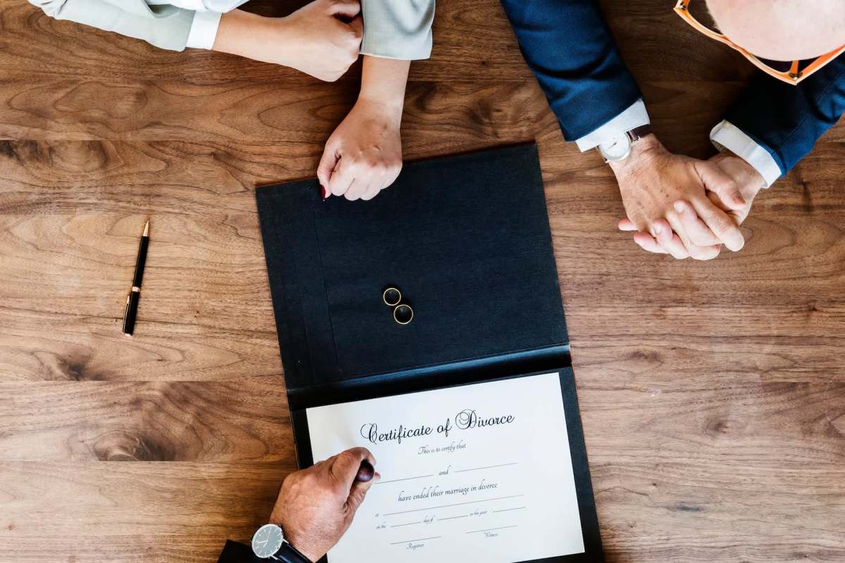 A certificate of divorce on a table with two wedding rings and hands clasped together.
