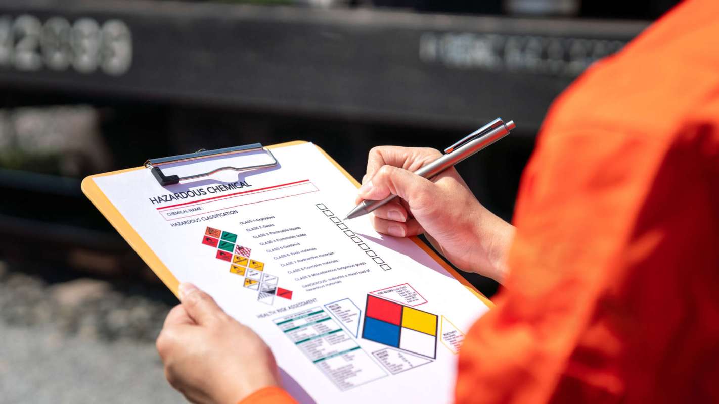 A person holds a clipboard with a hazardous chemical safety checklist and a pen.