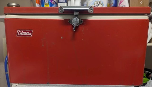 A red Coleman cooler with a metal latch in a cluttered storage area.