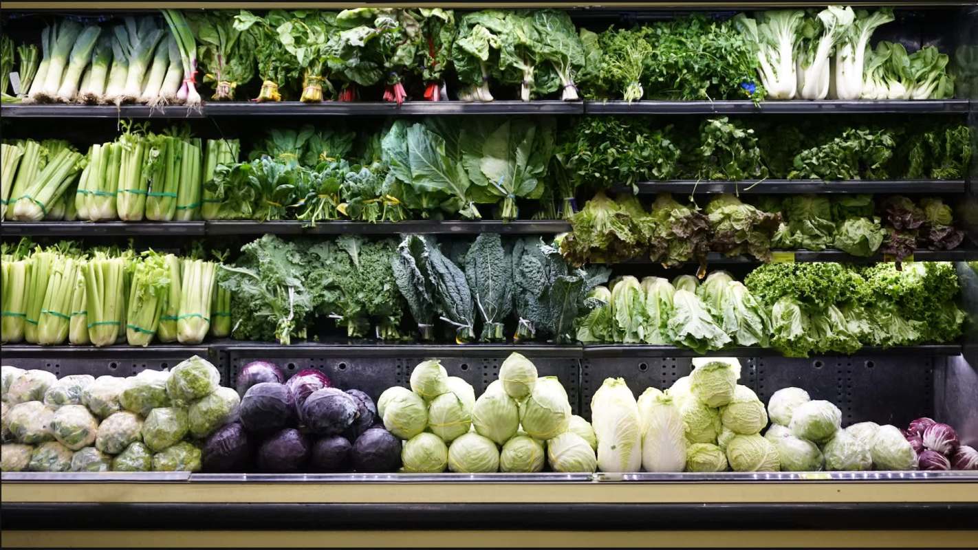 A display of various fresh green vegetables including lettuce, kale, and celery in a grocery store.