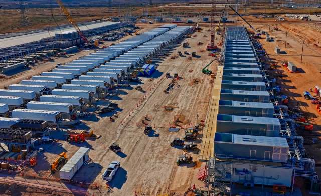 An aerial view of a data center construction site with rows of white containers and heavy machinery.
