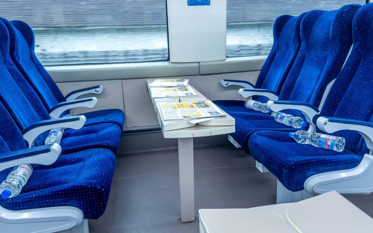 An interior view of a train carriage with blue seats, a table, and several water bottles.