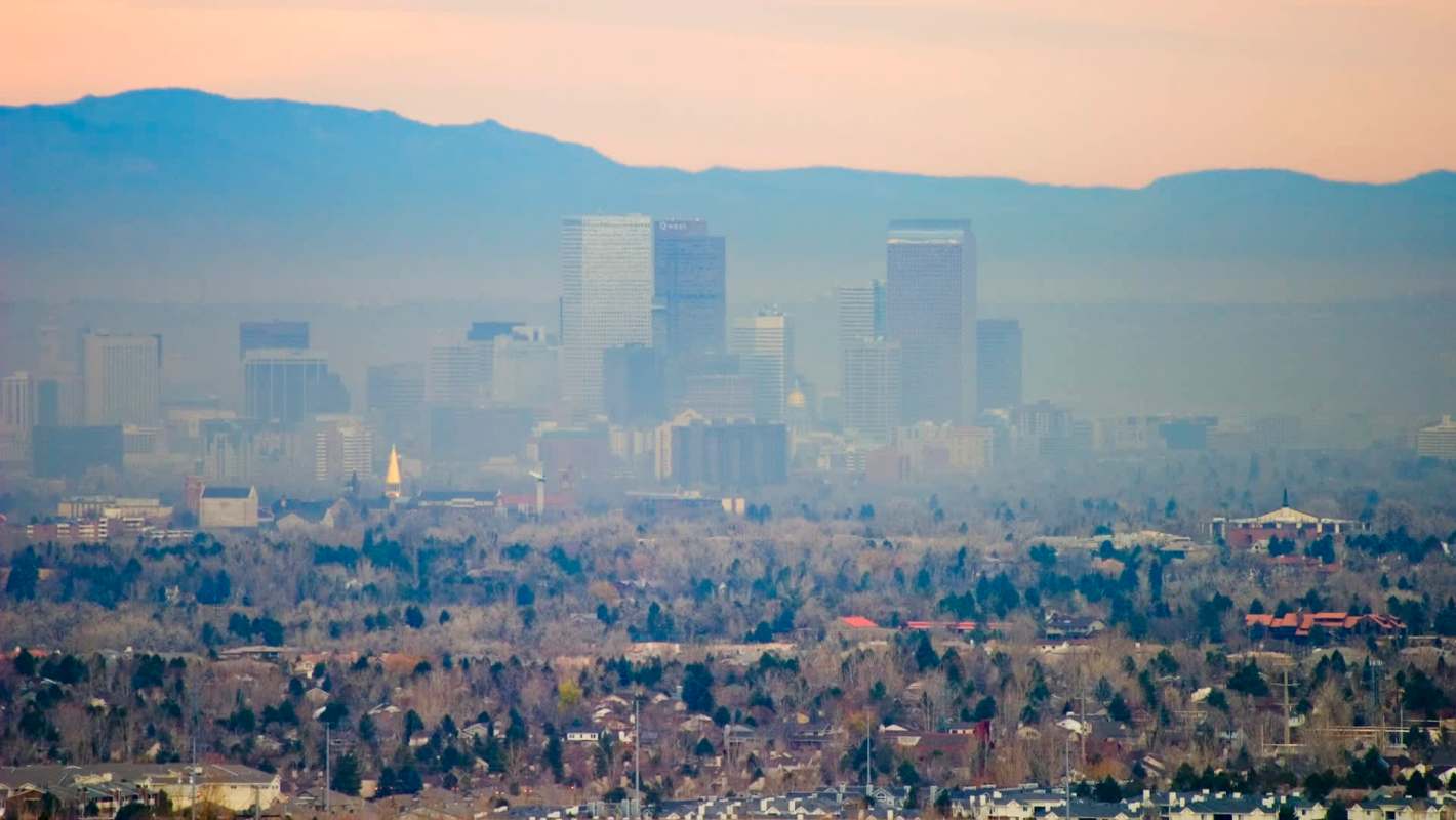 A view of the Denver, Colorado, skyline with smog, buildings and mountains in the background.
