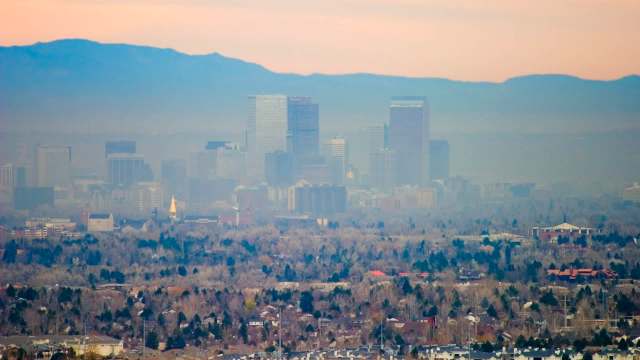 A view of the Denver, Colorado, skyline with smog, buildings and mountains in the background.