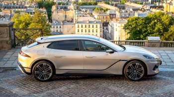 A silver Denza Z9 GT electric car parked on a cobblestone street with a city view in the background.