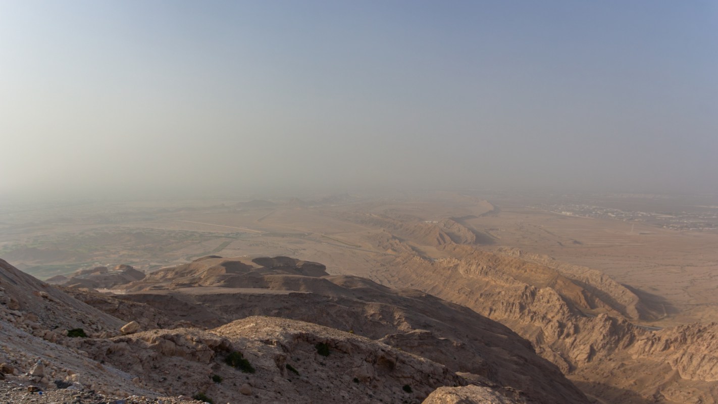 A panoramic view of a dry, rocky landscape with distant hills under a hazy sky.