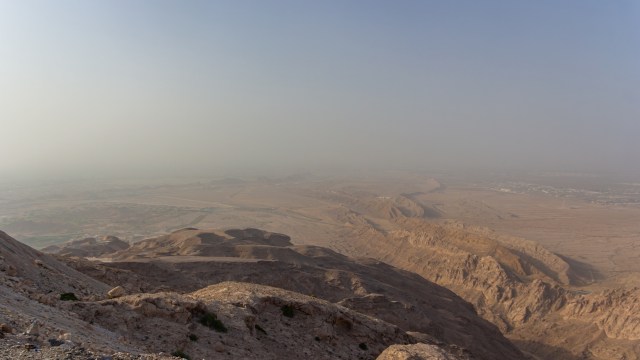 A panoramic view of a dry, rocky landscape with distant hills under a hazy sky.