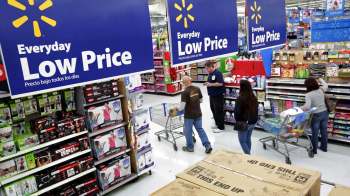 A retail store aisle with "Everyday Low Price" signs and shoppers with carts exploring various products.