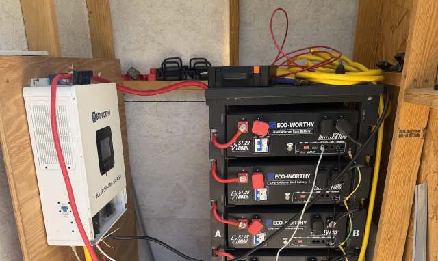 A solar inverter connected to multiple batteries in a utility shed.