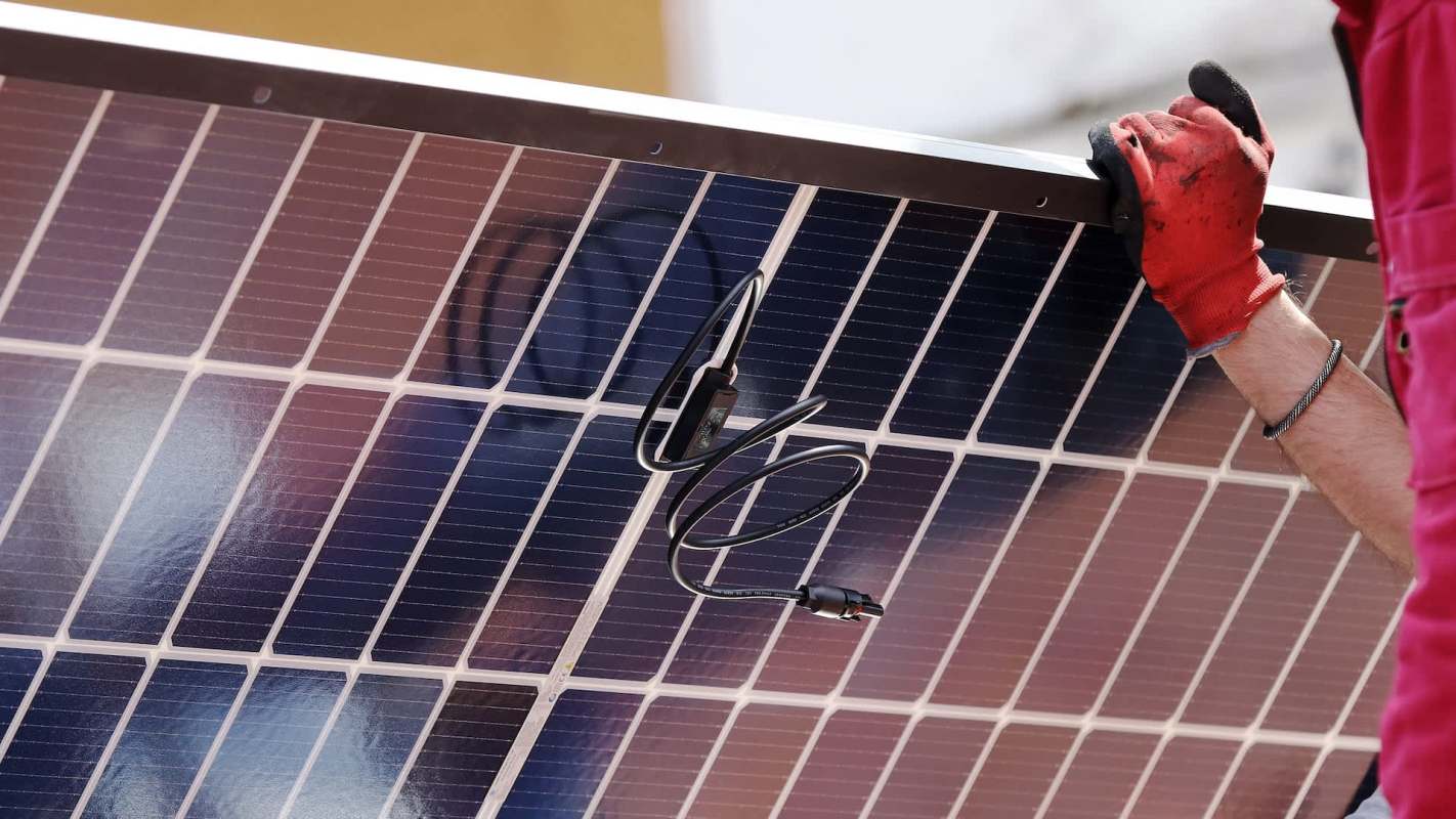 A person in gloves holds a solar panel with visible wiring.