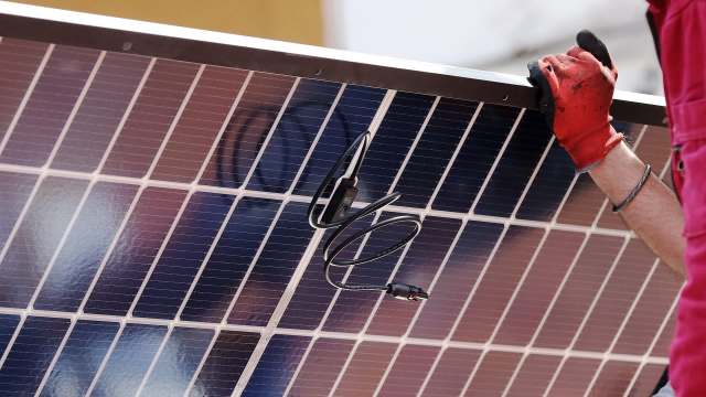 A person in gloves holds a solar panel with visible wiring.