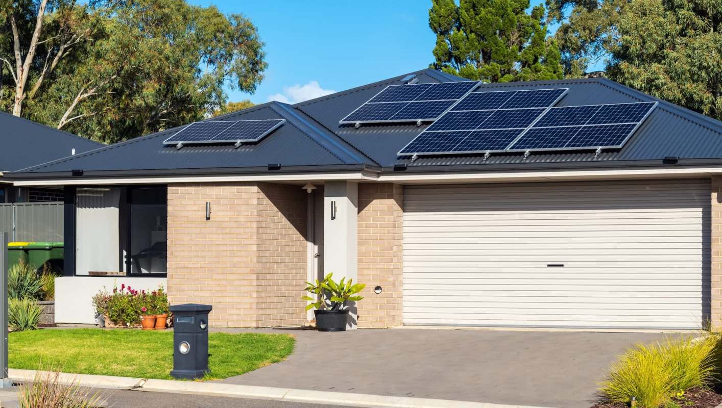 A modern house with solar panels on the roof and a small garden in front.