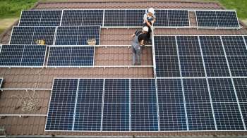 Two workers install solar panels on a tiled roof.