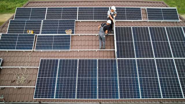 Two workers install solar panels on a tiled roof.