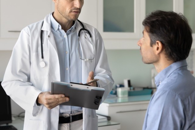 A doctor discusses information with a male patient in a medical office.