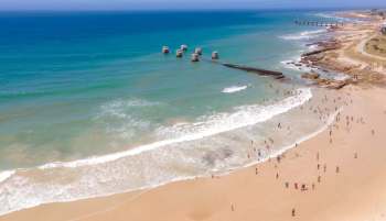 A beach scene with people wading in the water and several concrete pillars in the ocean.