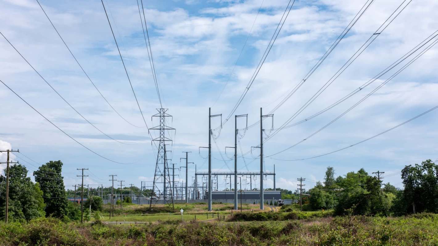 Power lines and transmission towers are visible in an open area with a cloudy sky in the background.